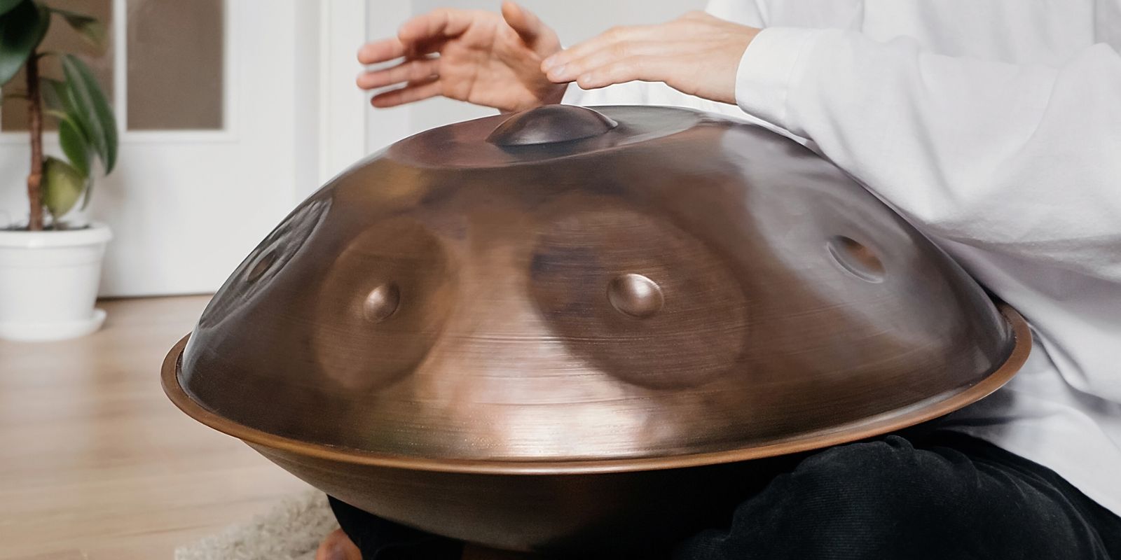 Man sitting cross-legged playing a handpan in a clean indoor sound therapy studio, illustrating a beginner-friendly handpan setup