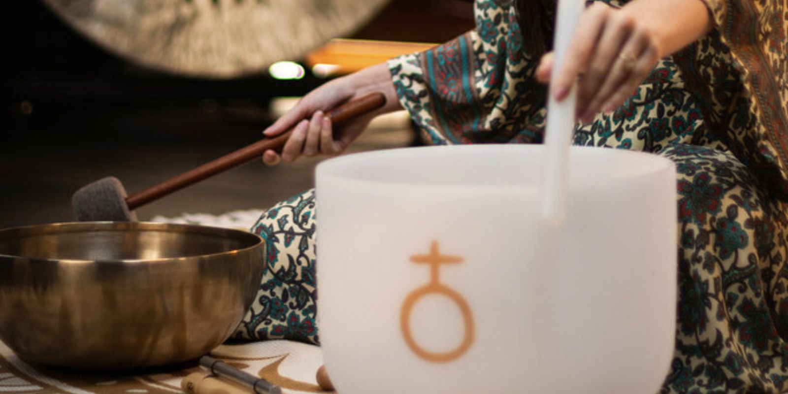 Woman playing singing bowls on a Meinl Sonic Energy rug during meditation and frequency practice