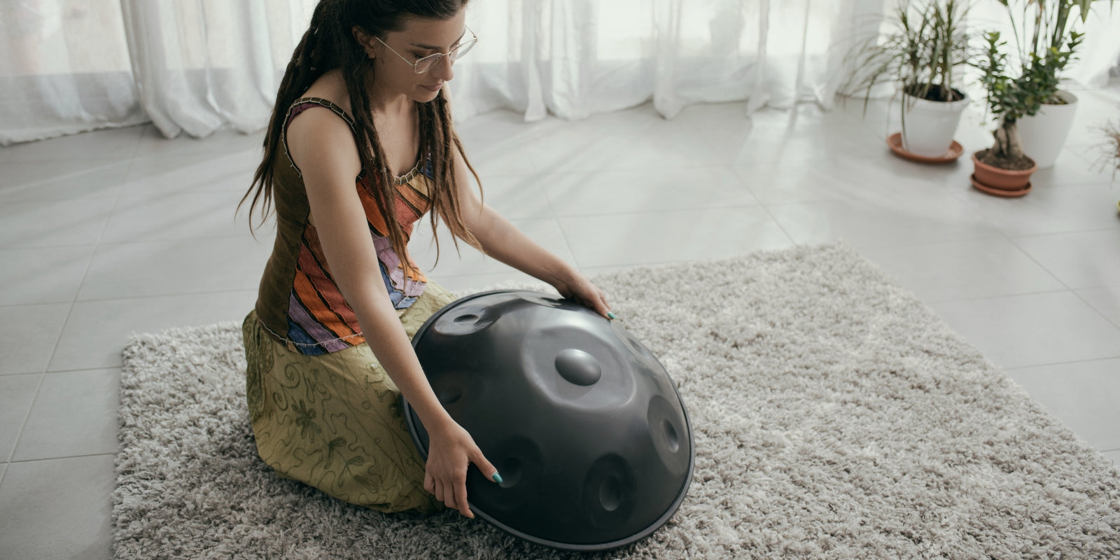 Woman kneeling on a mat holding a handpan in a calm indoor sound healing setting, illustrating a meditation instrument alternative to crystal singing bowls