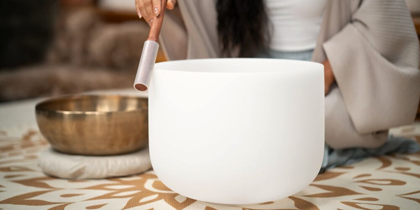 Close-up of a crystal singing bowl being played beside a traditional metal singing bowl during a sound healing session, comparing meditation frequency instruments
