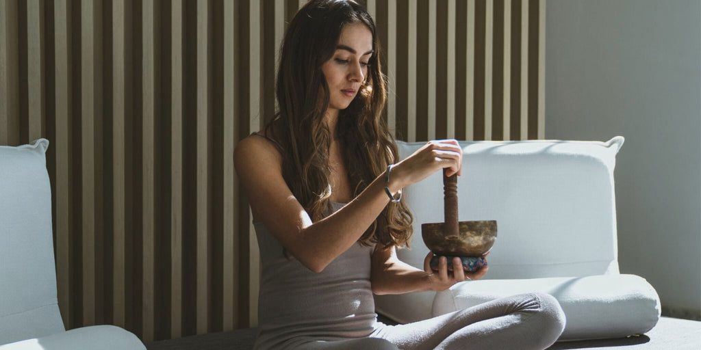 Woman holding and playing a metal singing bowl in a yoga meditation setting, demonstrating a traditional sound healing instrument for beginners