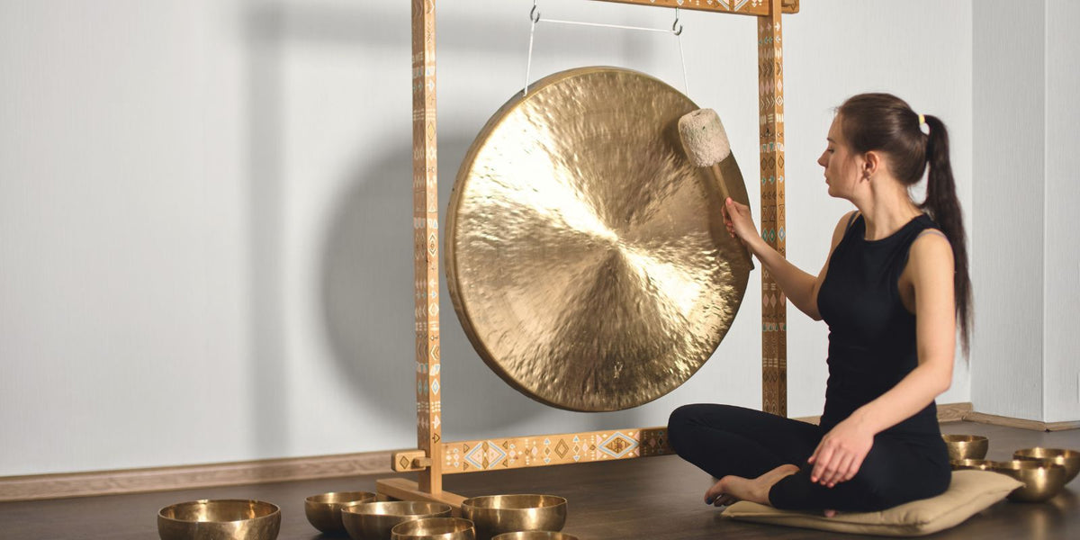Person playing a large gong with a mallet, exploring resonance, vibration and immersive sound.