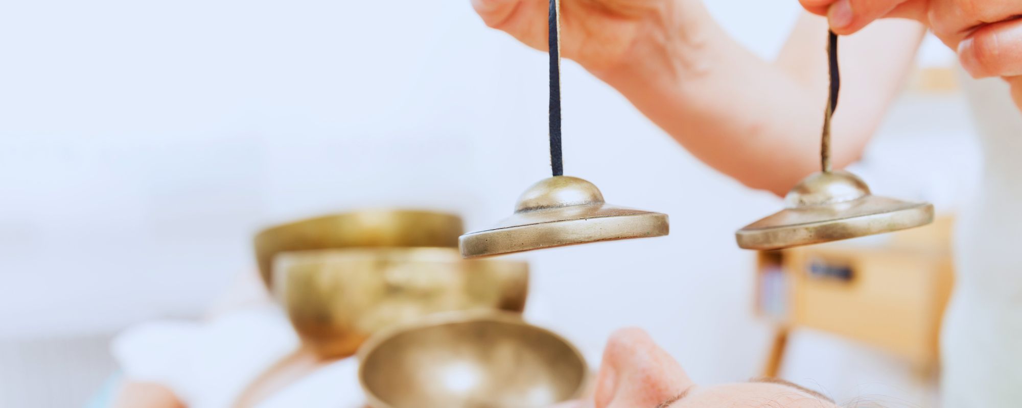 Sound therapist using hand cymbals and Tibetan tingshas above a woman’s face during a calming sound healing therapy session.