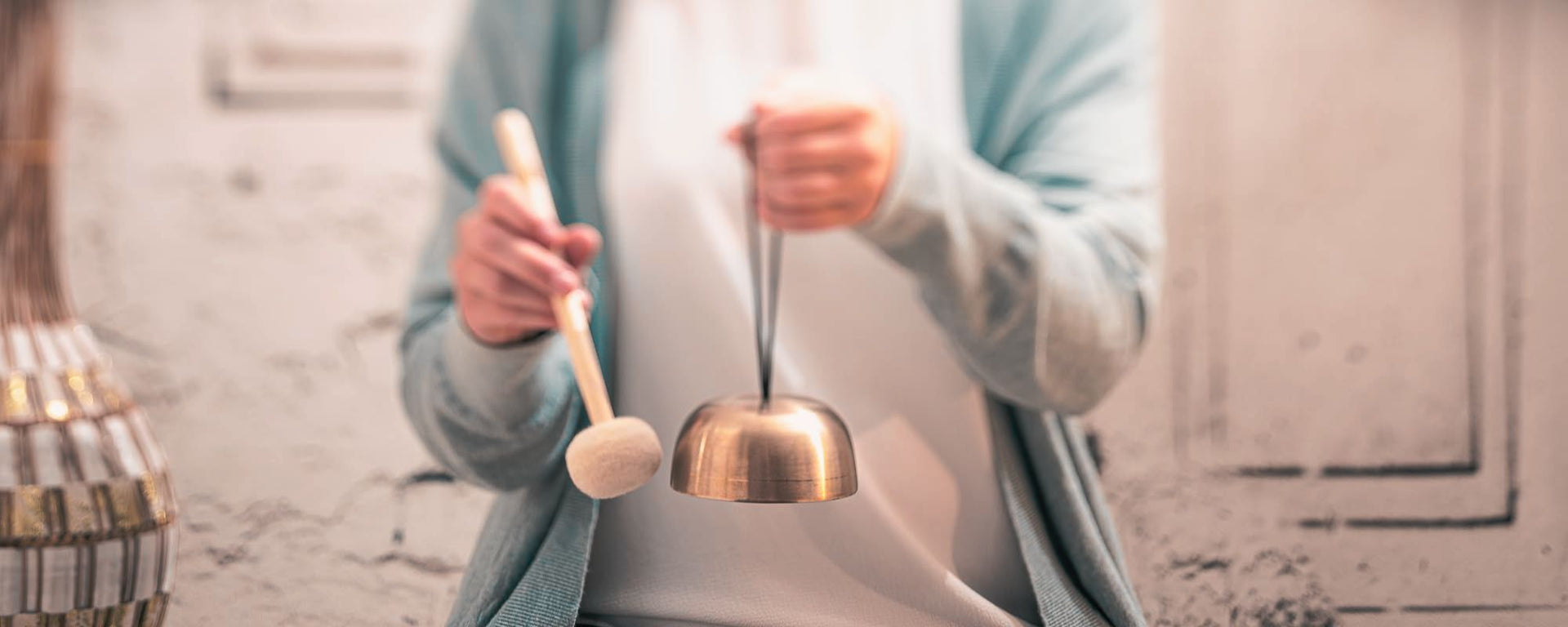 Sound therapist using a mallet to play a singing bowl above a woman’s face during a calming sound healing therapy session.