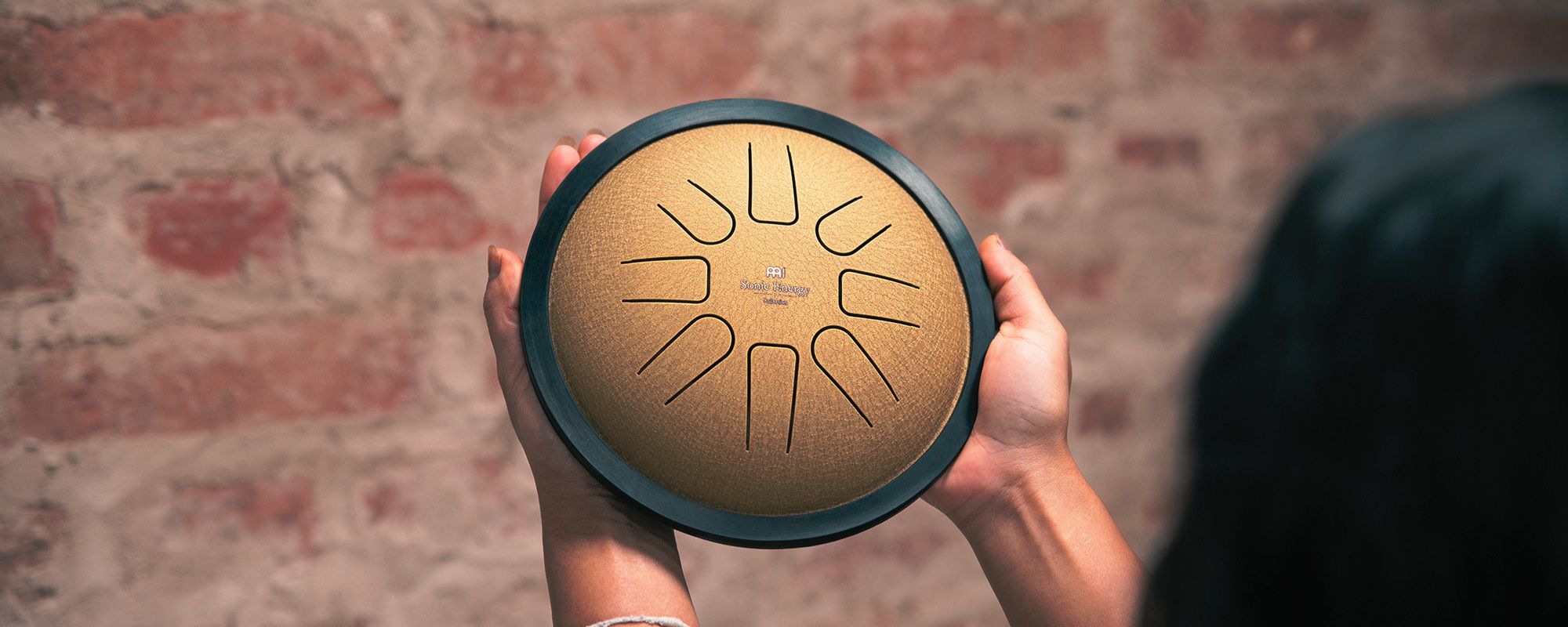 Woman holding a Meinl Sonic Energy tongue drum with both hands, showcasing the instrument’s calming tones for sound healing and relaxation.
