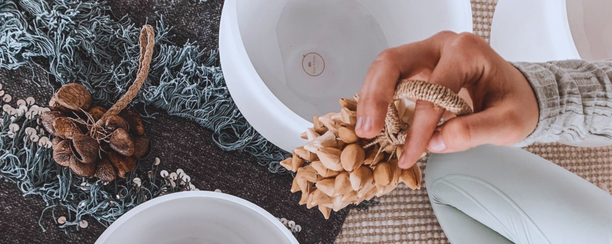 Sound therapist using a kenari shaker in a healing session, surrounded by singing bowls and percussion instruments on the floor.