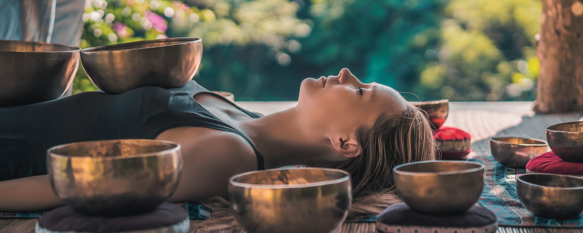 Woman lying in a sound healing session surrounded by metal singing bowls, creating calming vibrations for relaxation, meditation, and energy balancing.