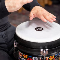 Musician playing the Meinl Jumbo Series Djembe Drum 10" Day of the Dead JD10DA, demonstrating its hand-played percussion style and synthetic drumhead.