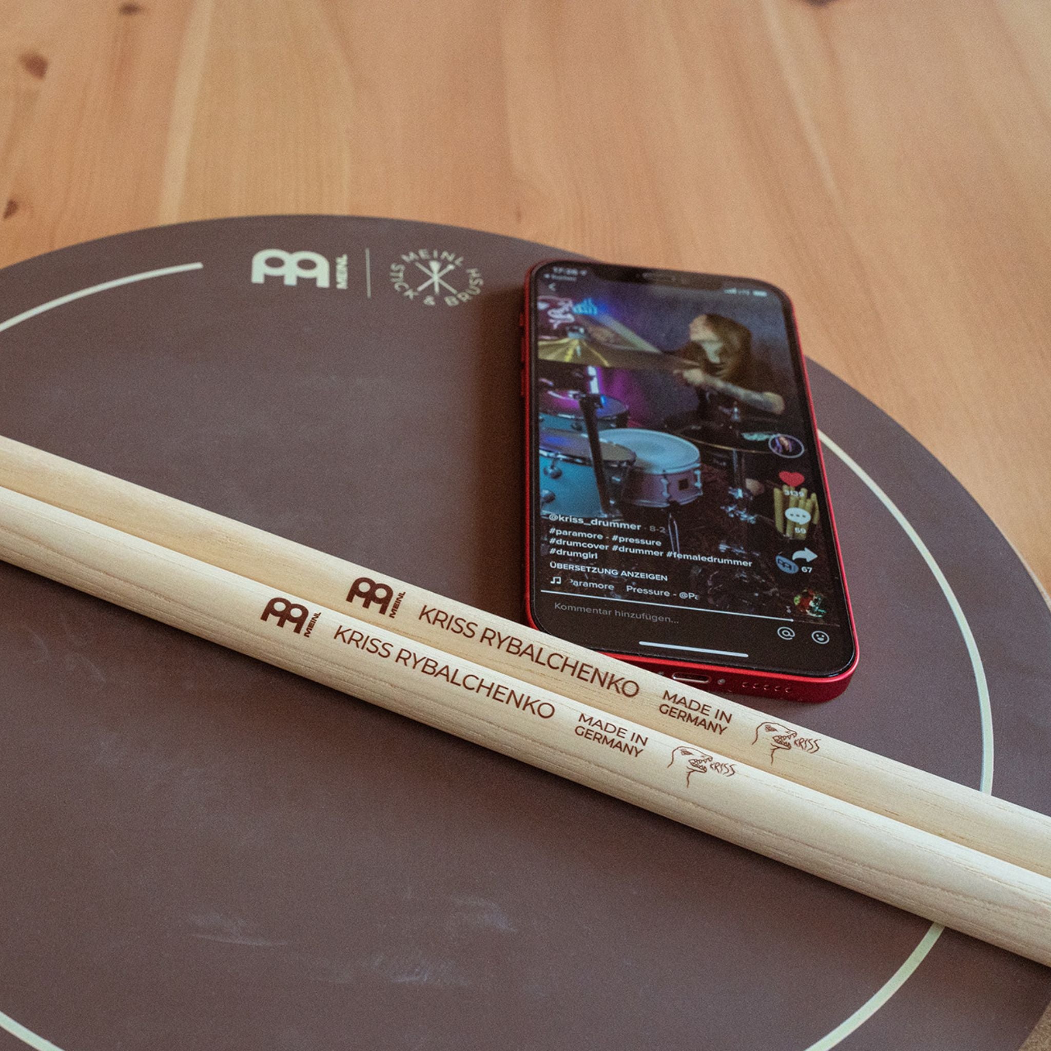 Meinl Kriss Rybalchenko Signature Drumsticks SB603 resting on a Meinl practice pad beside a smartphone, ready for practice and technique development.