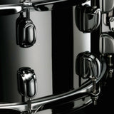 Close-up side view of the Tama S.L.P. Black Brass Snare Drum LBR1465 showing the 1.5mm brass shell, Black Nickel Starclassic lugs, and strainer hardware.
