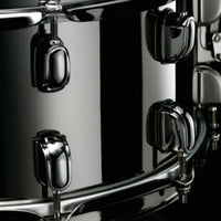 Close-up side view of the Tama S.L.P. Black Brass Snare Drum LBR1465 showing the 1.5mm brass shell, Black Nickel Starclassic lugs, and strainer hardware.