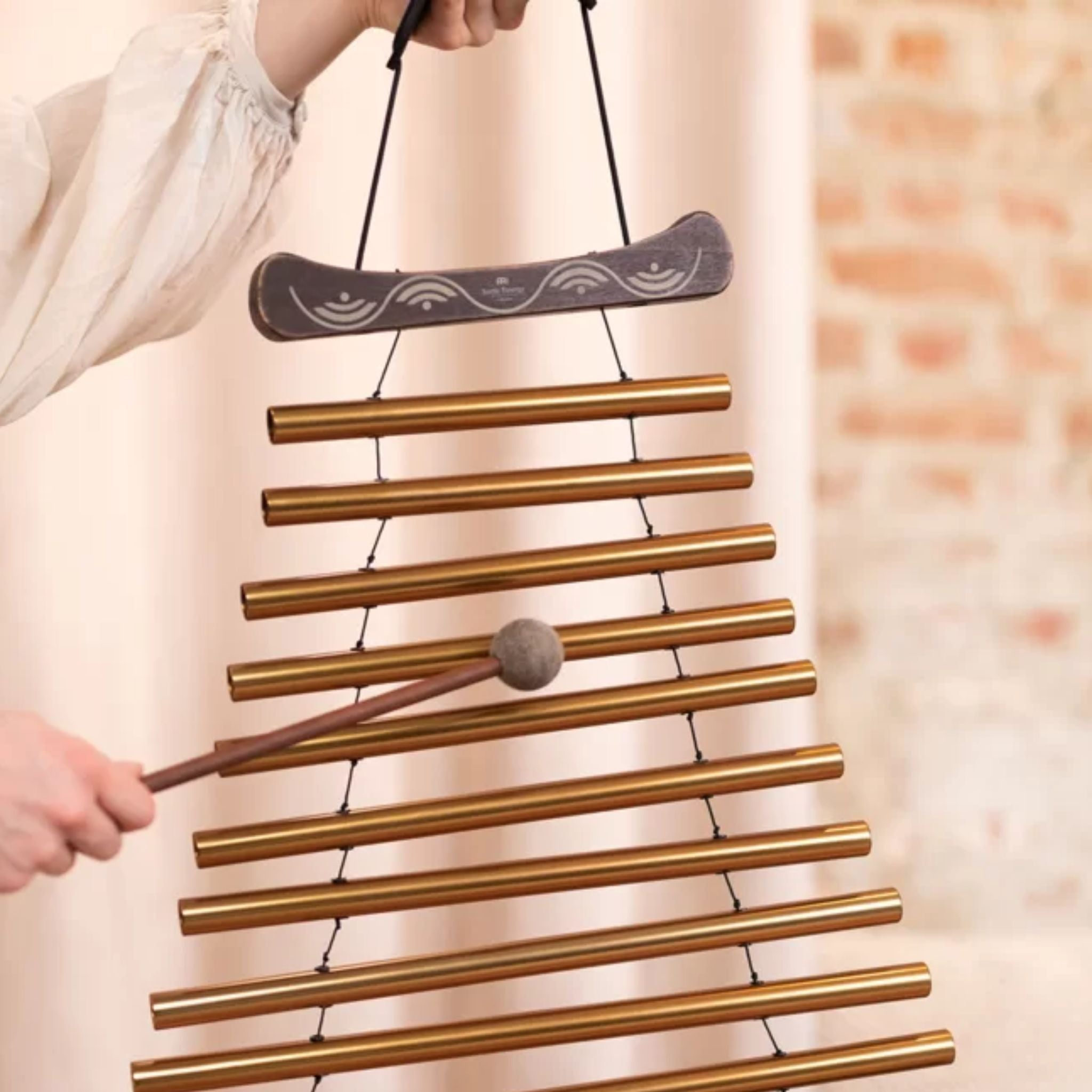 Close-up of the Meinl Sonic Energy Meditation Flow Chime 88cm 440Hz D Major Bronze MFC10DMAB being held inverted and played by hand with the included mallet.