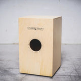 Wooden cajon drum with 'Snarecraft' branding on a gray surface.