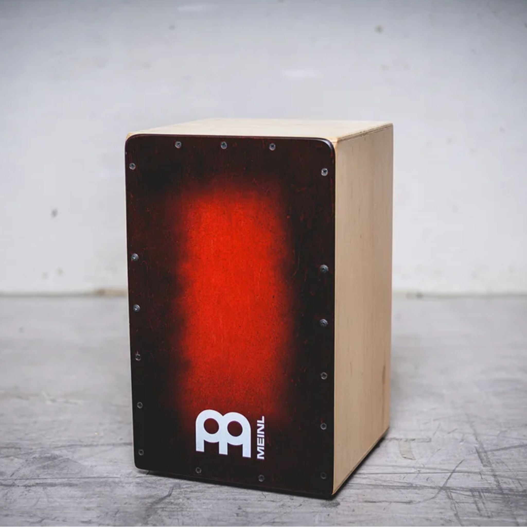 Cajon drum with red front panel and Meinl logo on a gray surface