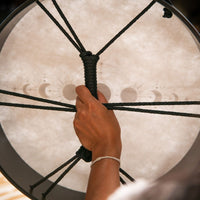 Rear view of the Meinl Sonic Energy Ritual Drum 16" Moon Phases RD16DWB-SH being held by the cord cross grip, showing the dark walnut brown poplar frame.