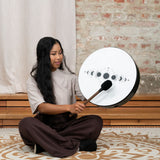 Woman seated and playing the Meinl Sonic Energy Ritual Drum 16" Moon Phases RD16DWB-SH with the included mallet.