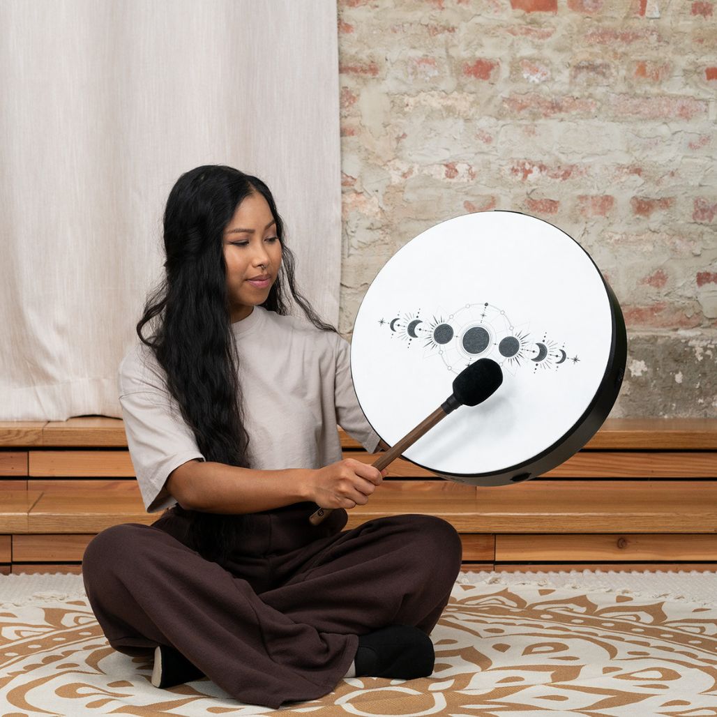 Woman seated and playing the Meinl Sonic Energy Ritual Drum 16" Moon Phases RD16DWB-SH with the included mallet.
