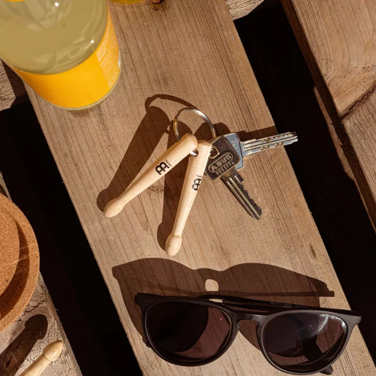 Meinl Drumstick Keyring SB506 with miniature maple drumsticks on a wooden table alongside sunglasses and drinks.