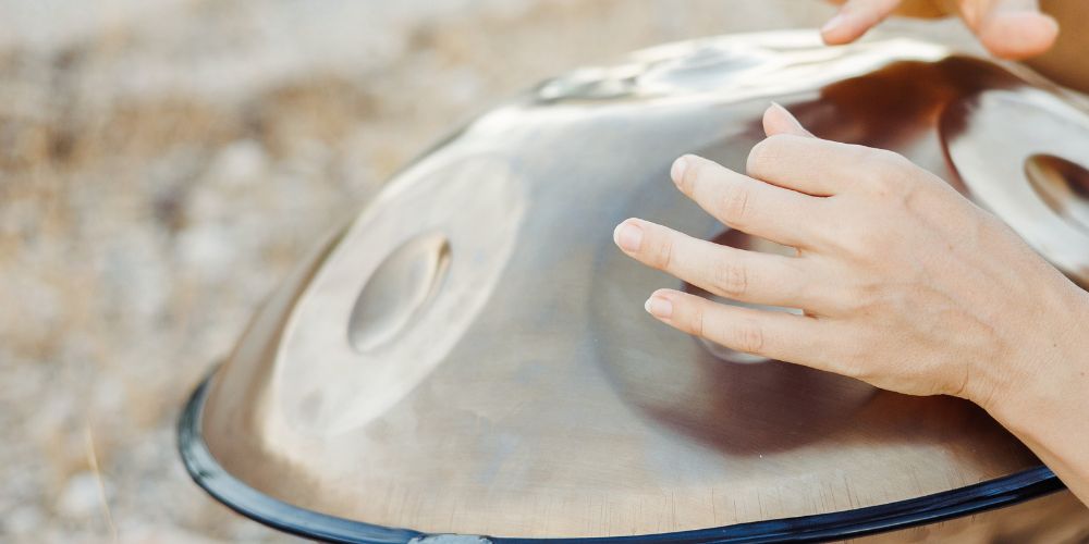 Close-up of woman’s hands playing a handpan in warm golden light during a sound healing session, creating immersive resonant tones