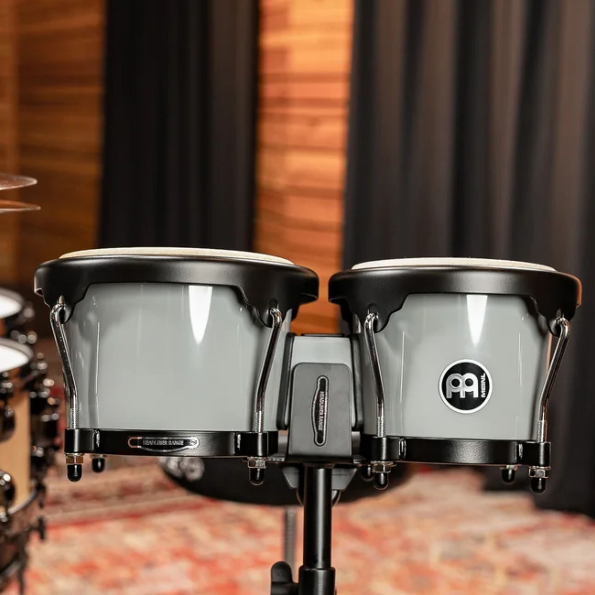 Meinl Journey Series bongo drums in Ultimate Gray (HB50UG), mounted on stand in a professional studio setting with warm acoustic backdrop.