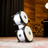 Meinl Journey Series bongo drums in white finish, stacked upright in a studio environment, showcasing compact form, black rims, and natural drumheads.