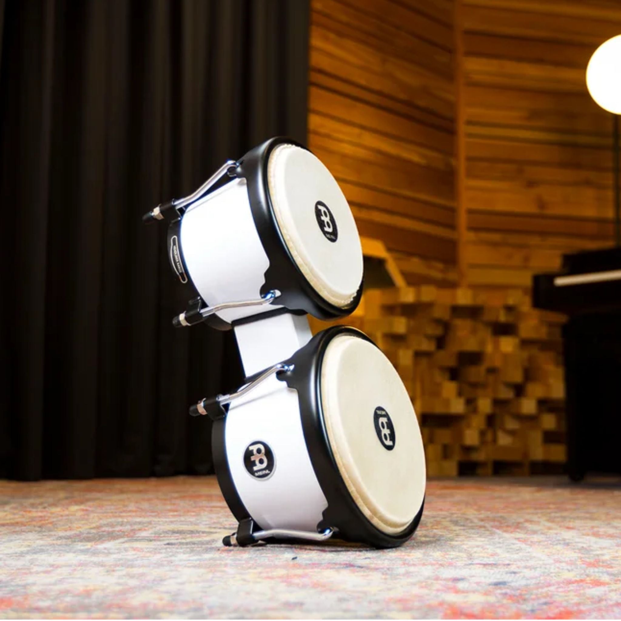 Meinl Journey Series bongo drums in white finish, stacked upright in a studio environment, showcasing compact form, black rims, and natural drumheads.