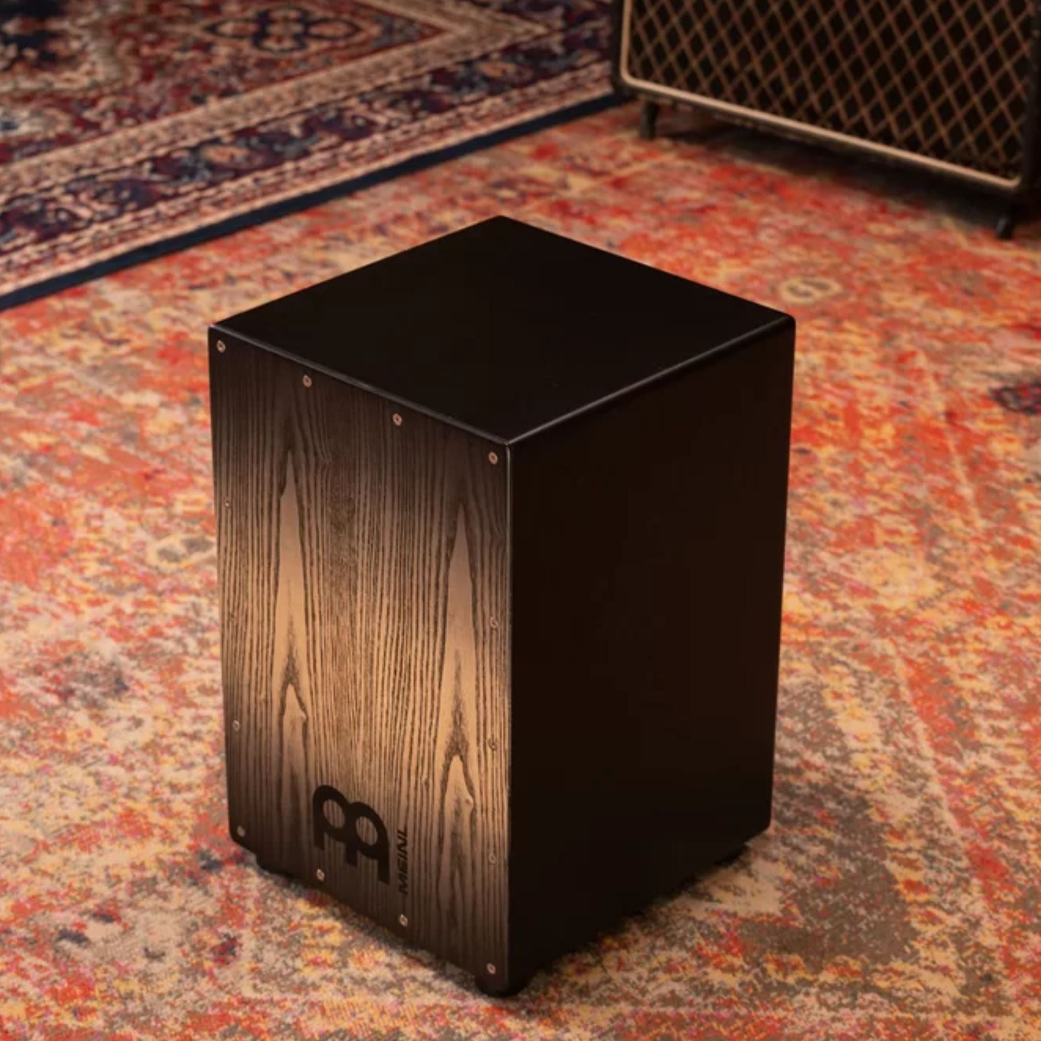 Angled side view of the Meinl Headliner Series Snare Cajon MCAJ100BK-CBF in a rustic studio setting, highlighting its Charcoal Black Fade finish and refined build quality
