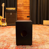 Front view of the Meinl Headliner Series Snare Cajon MCAJ100BK-CBF in a rustic studio environment, showcasing its Charcoal Black Fade finish and professional presence