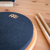 Meinl Marshmallow Practice Pad 12 inch in orange (MMP12OR), close-up detail of textured foam playing surface and rim with drumsticks nearby on a wooden desk.