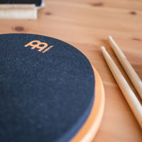 Meinl Marshmallow Practice Pad 12 inch in orange (MMP12OR), close-up detail of textured foam playing surface and rim with drumsticks nearby on a wooden desk.