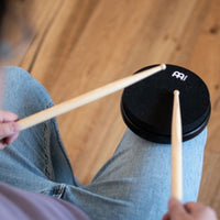 Person playing the Meinl Marshmallow Practice Pad 6" Black MMP6BK on their knee with a pair of drumsticks.