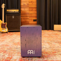 Front view of the Meinl Snare Cajon Headliner Series Lilac Purple Fade MCAJ100BK-LPF in a rustic studio setting — premium percussion drum for professional performance and recording.