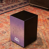 Side view of the Meinl Snare Cajon Headliner Series Lilac Purple Fade MCAJ100BK-LPF in a rustic studio setting — showcasing front, side, and top with premium craftsmanship for professional performance.