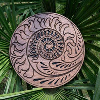 10 inch rain disk resting outdoors on palm tree branch showing Fibonacci-inspired carved surface in natural environment