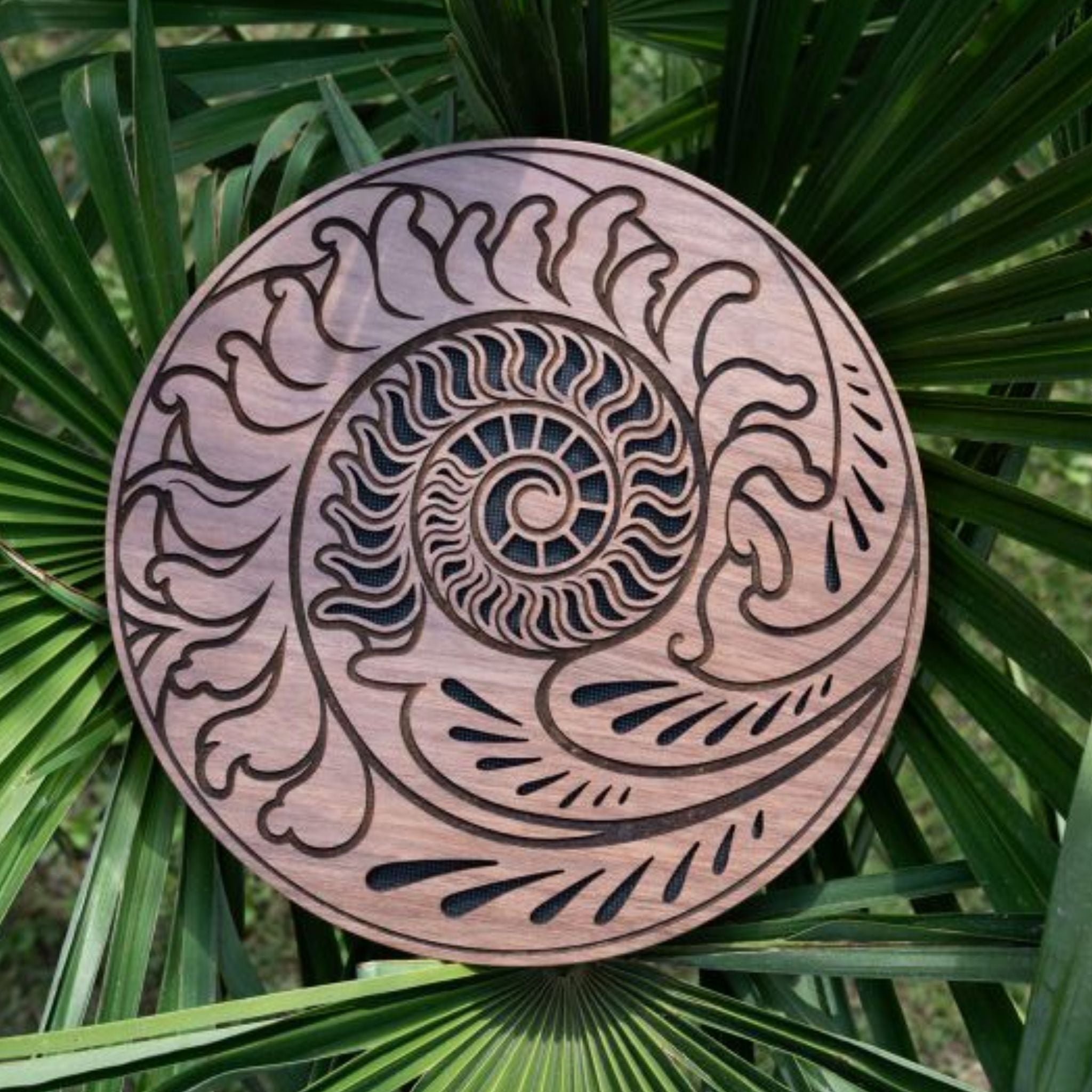 10 inch rain disk resting outdoors on palm tree branch showing Fibonacci-inspired carved surface in natural environment