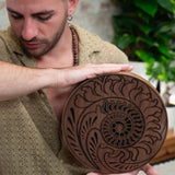 close up of man playing 10 inch rain disk during sound therapy session showing rotational hand movement and Fibonacci-inspired carved surface detail