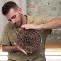 man playing 10 inch rain disk while seated cross legged during sound therapy session creating calming ocean-like resonance