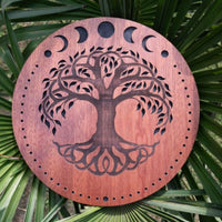 12 inch rain disk resting outdoors on palm tree branch showing carved Moon Phases and Tree of Life surface in natural environment