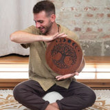 man playing 12 inch rain disk while seated cross legged during sound therapy session creating calming water-like resonance