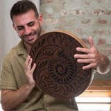 close up of man playing 15 inch rain disk during sound therapy session showing rotational hand movement and Fibonacci-inspired carved surface detail