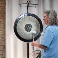 close up of man playing the Meinl Sonic Energy 24 inch Flower of Life Soundscape Gong 64Hz GFOL24 on a gong stand, highlighting the engraved Flower of Life design, polished nickel silver surface, and immersive resonant sound.