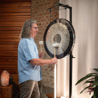 man playing the Meinl Sonic Energy 24 inch Flower of Life Soundscape Gong 64Hz GFOL24 suspended from a gong stand, demonstrating immersive resonance, dynamic overtones, and expressive sound for meditation, sound therapy, and wellness practices.