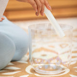 close up of woman playing the 6 inch E4 Clear Solar Plexus Crystal Singing Bowl from the Meinl Sonic Energy 3-Piece Essence Crystal Singing Bowl Set ECSBSETECG using a crystal silicone rod to create rich resonant tones and long-lasting harmonic vibrations