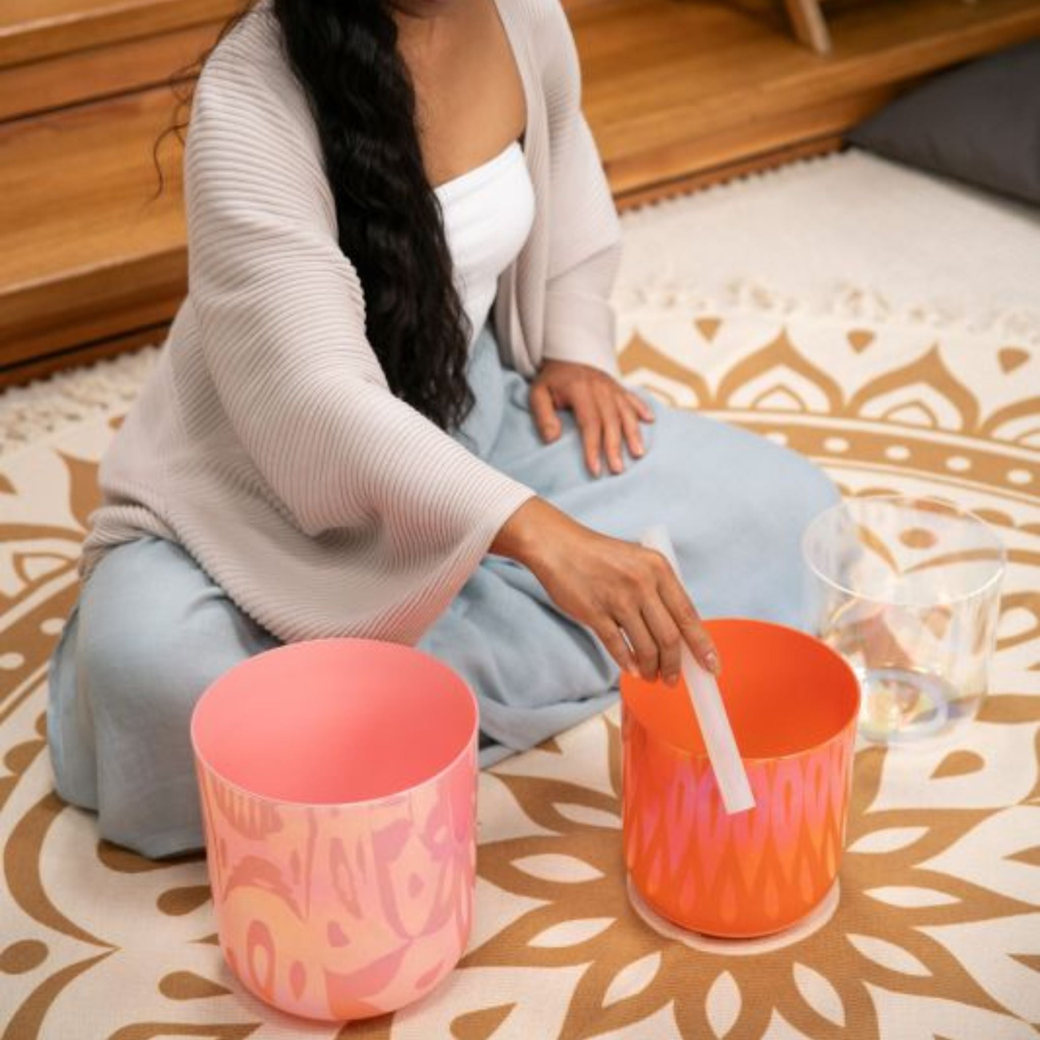 woman playing the Meinl Sonic Energy 3-Piece Essence Crystal Singing Bowl Set E4 C4 G3 440Hz ECSBSETECG on a meditation rug, creating harmonic quartz crystal tones for meditation, sound therapy, and immersive sound exploration