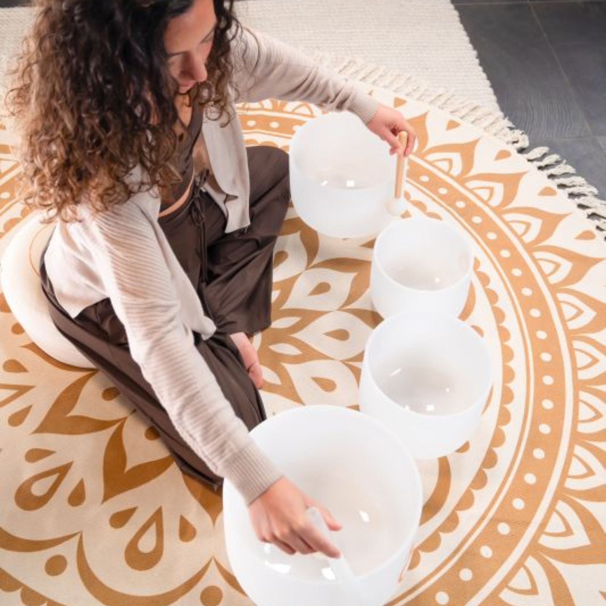 aerial view of woman playing Meinl Sonic Energy 4-Piece Om Crystal Singing Bowl Set CSBSETOM4 on meditation rug showing four white frosted quartz crystal singing bowls arranged for meditation, sound therapy, and immersive sound exploration sessions