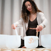 woman playing Meinl Sonic Energy 4-Piece Om Crystal Singing Bowl Set CSBSETOM4 on meditation rug creating resonant quartz crystal tones for meditation, sound therapy, and mindfulness practice