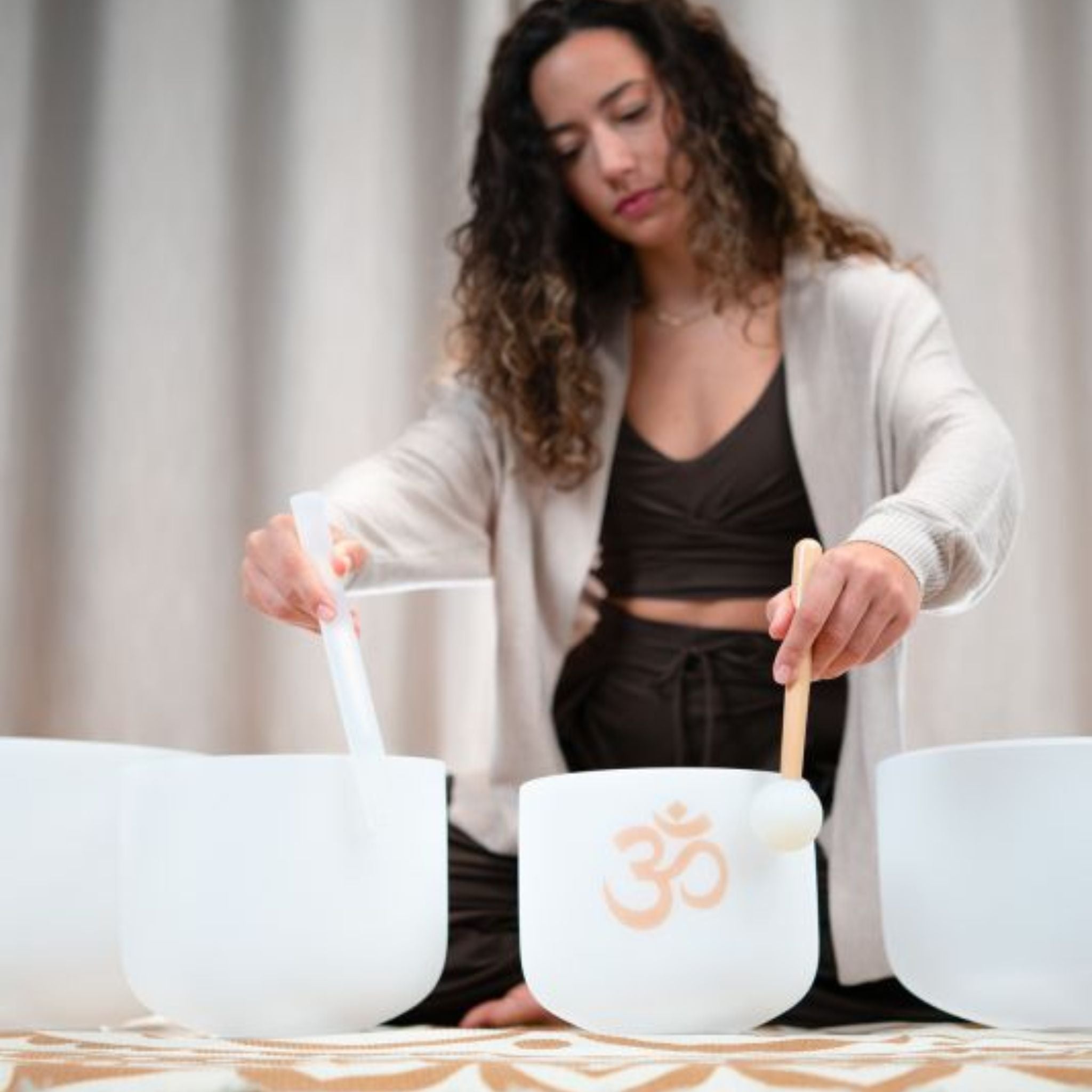woman playing Meinl Sonic Energy 4-Piece Om Crystal Singing Bowl Set CSBSETOM4 on meditation rug creating resonant quartz crystal tones for meditation, sound therapy, and mindfulness practice