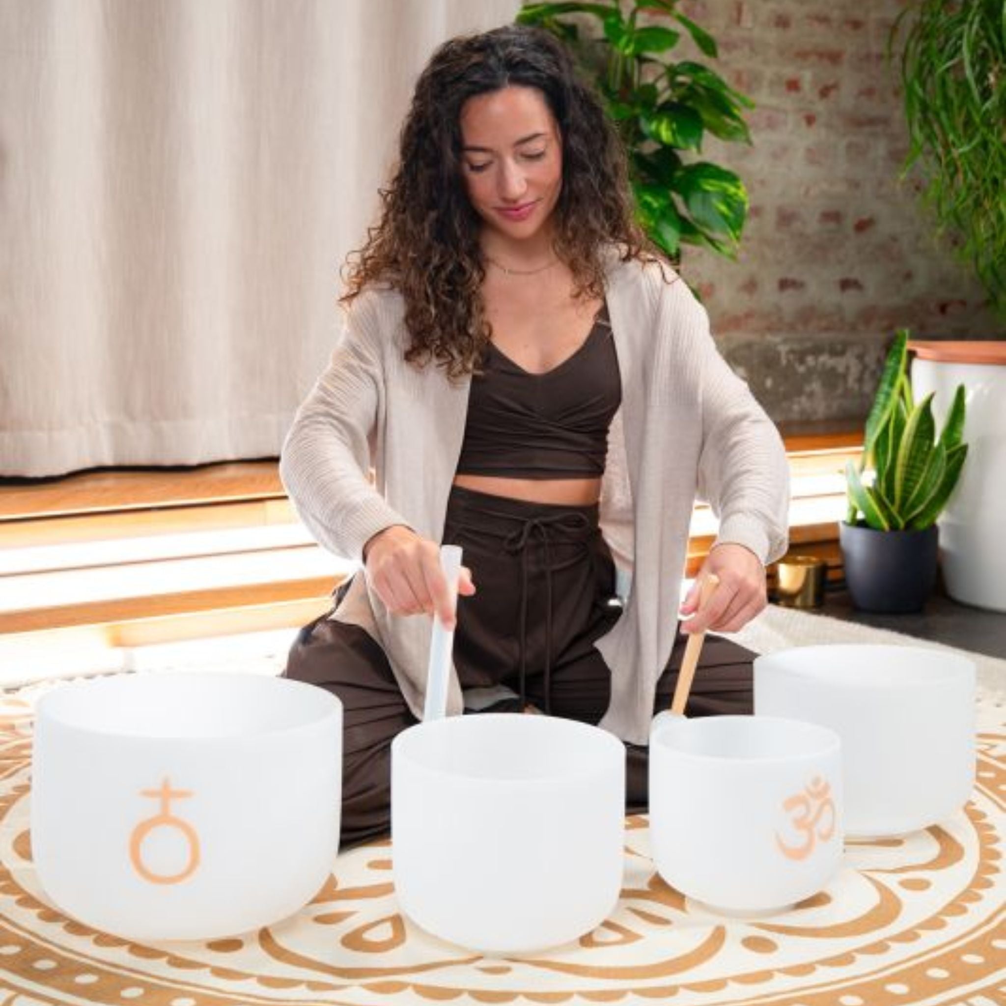 woman playing Meinl Sonic Energy 4-Piece Om Crystal Singing Bowl Set CSBSETOM4 on meditation rug creating immersive crystal bowl soundscapes and harmonic resonance for relaxation and mindfulness