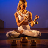 woman sitting cross-legged on a yoga mat with the Meinl Sonic Energy 4-Piece Universal Series Singing Bowl Set SB-U-1750 arranged in front of her while holding the smallest singing bowl and suede mallet for meditation, mindfulness, and sound therapy practice.