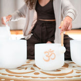 close up of woman playing Meinl Sonic Energy 6-Piece Om Crystal Singing Bowl Set CSBSETOM6 showing white frosted quartz crystal singing bowls, mallet technique, and resonant tones used for meditation, sound therapy, and immersive sound exploration sessions